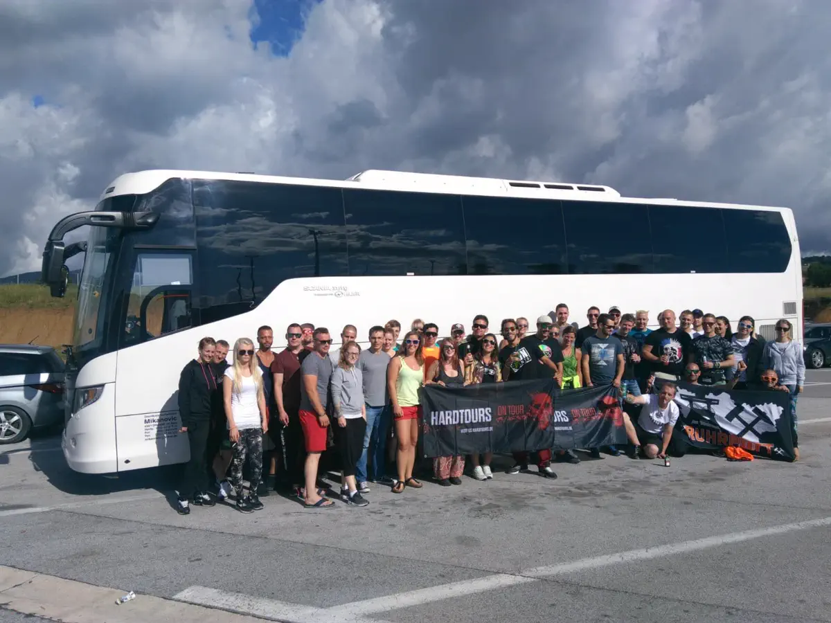 Reisegruppe mit Bannern vor einem weißen Reisebus von Mikanovic auf einem Parkplatz