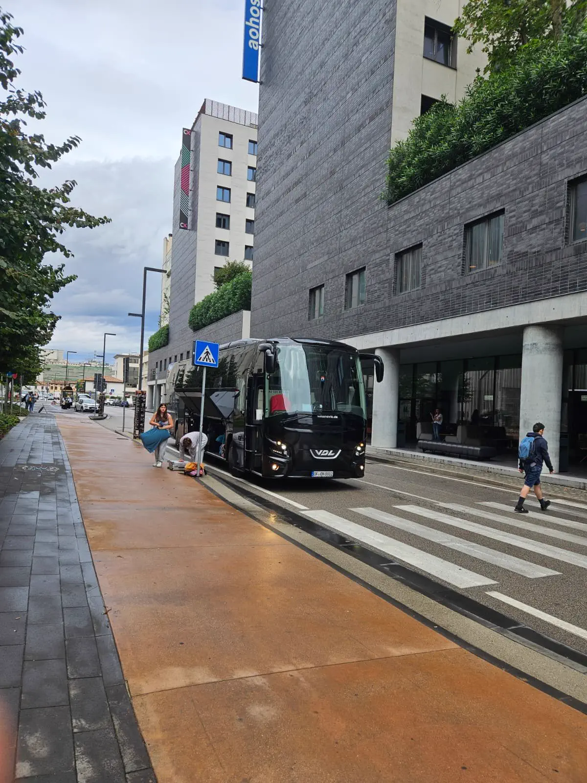 Schwarzer VDL-Reisebus mit geöffneter Gepäckklappe vor einem Hotel, Reisende holen ihr Gepäck