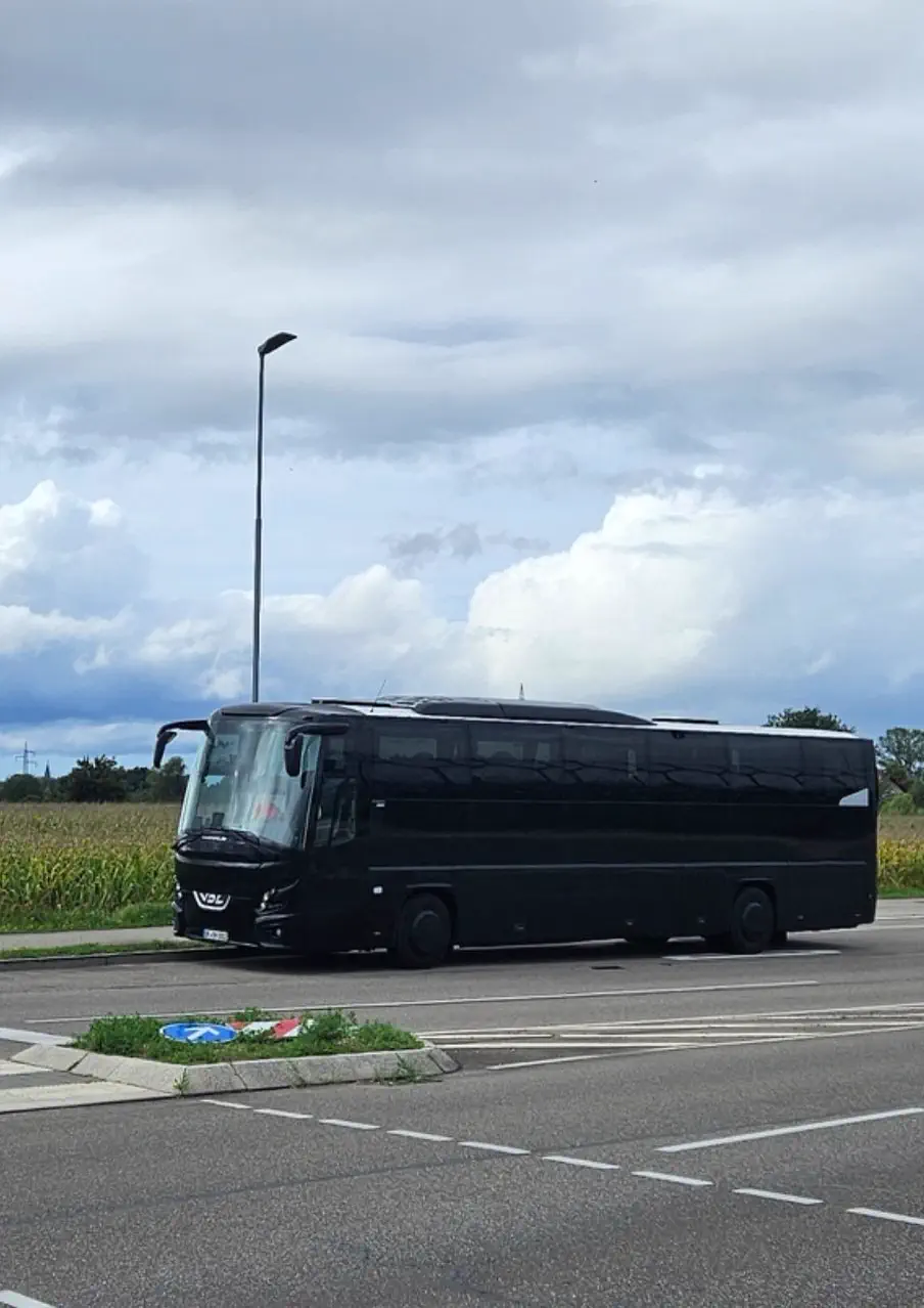 Schwarzer VDL-Reisebus am Straßenrand vor einem Feld unter bewölktem Himmel