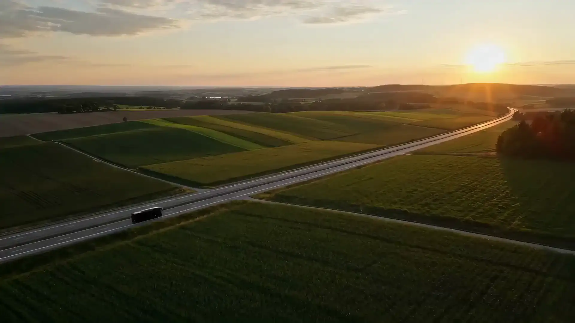 Reisebus auf einer Straße zwischen Feldern im Abendlicht, aus der Luft